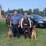 Two K9 handlers standing with their German Shepherd police service dogs beside patrol vehicles
