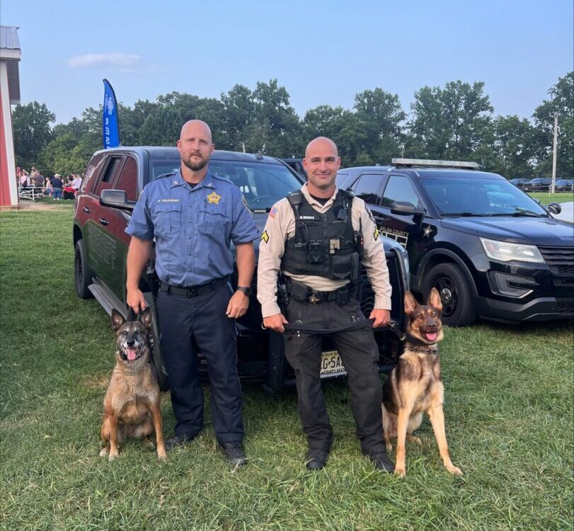 Two K9 handlers standing with their German Shepherd police service dogs beside patrol vehicles