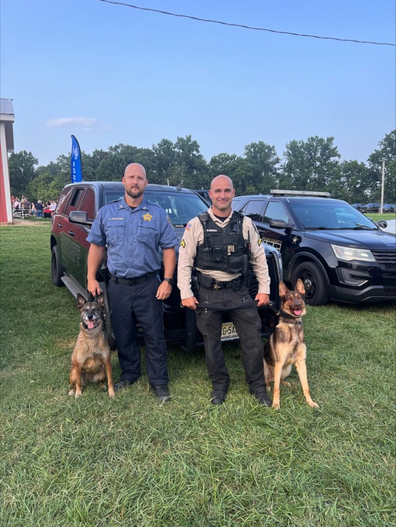 Two K9 handlers standing with their German Shepherd police service dogs beside patrol vehicles