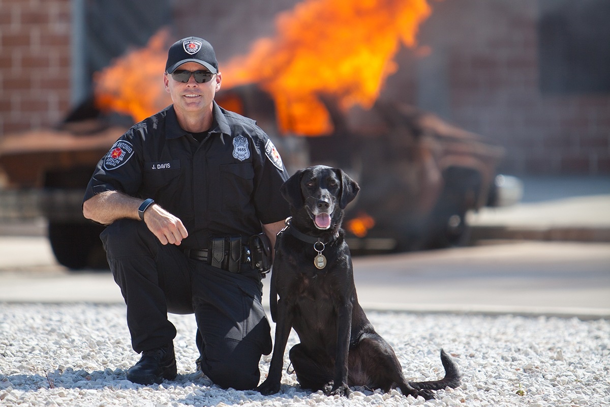 San Antonio arson investigator with a Fire K9 in front of a controlled burn.